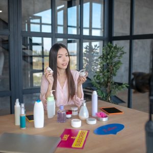 Woman with cream. Dark-haired appealing young woman recommending cream while filming blog